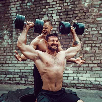 man lifting dumbbells with a spotter