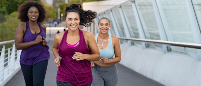 Happy women jogging together on city bridge