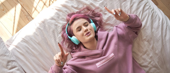 a girl laid on a bed with headphones on in a pink hoodie