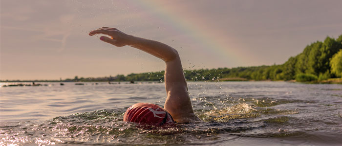 Woman swims in a lake in front of a rainbow